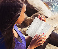 A woman by the water reading and studying passages from different translations of the Bible.